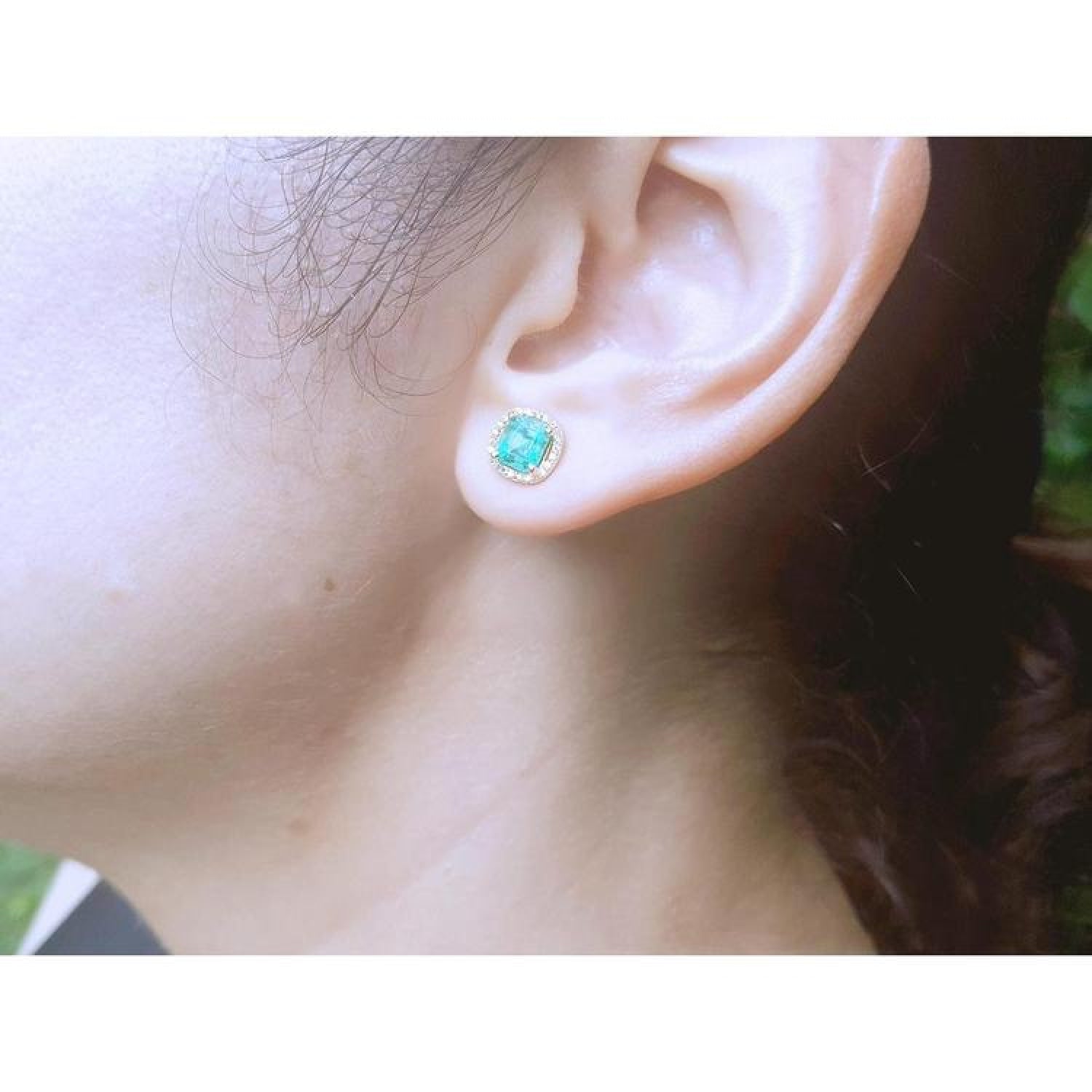 1.55 carat emerald stud earring with halo diamonds in 14K yellow gold on an ear.