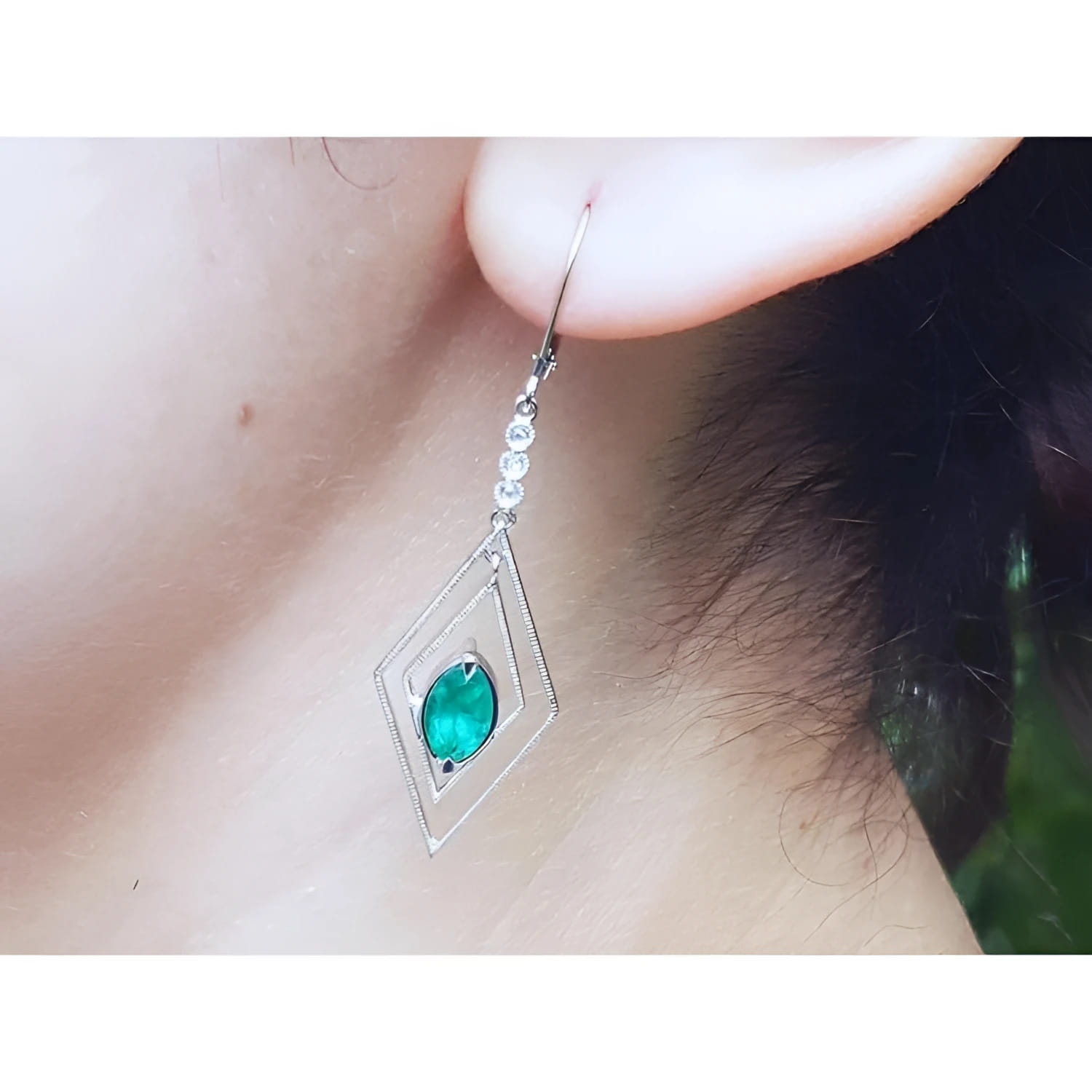 A diamond-shaped earring with a natural marquise emerald worn by a woman.
