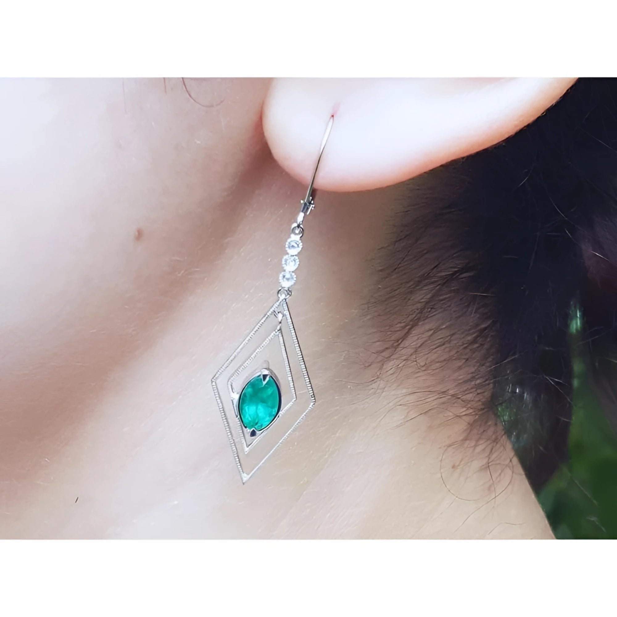 A diamond-shaped earring with a natural marquise emerald worn by a woman.