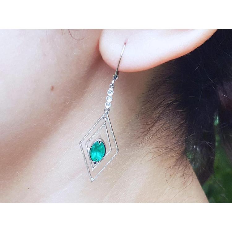 Close-up of a diamond-shaped earring with a marquise emerald worn by a woman.