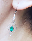 Close-up of a diamond-shaped earring with a marquise emerald worn by a woman.