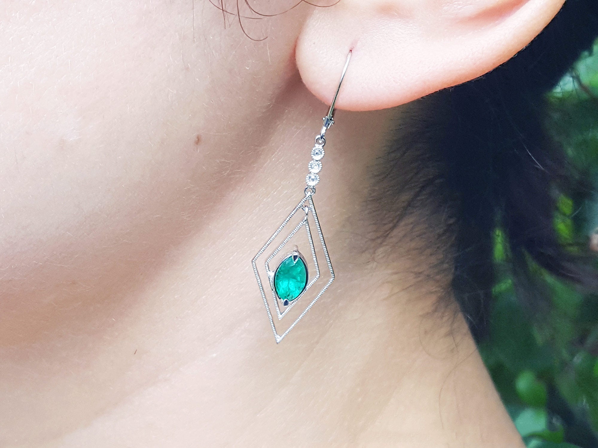 Close-up of an earring with a marquise cut emerald worn by a woman.