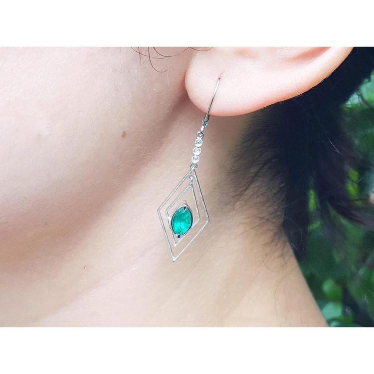 Close-up of an earring with a marquise cut emerald worn by a woman.