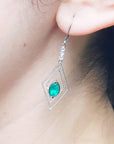 Close-up of an earring with a marquise cut emerald worn by a woman.