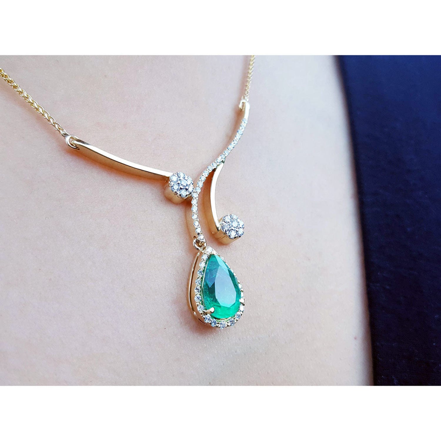 18K yellow gold necklace with a pear-shaped Colombian emerald pendant and diamond accents on a person's neck.