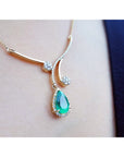 18K yellow gold necklace with a pear-shaped Colombian emerald pendant and diamond accents on a person's neck.