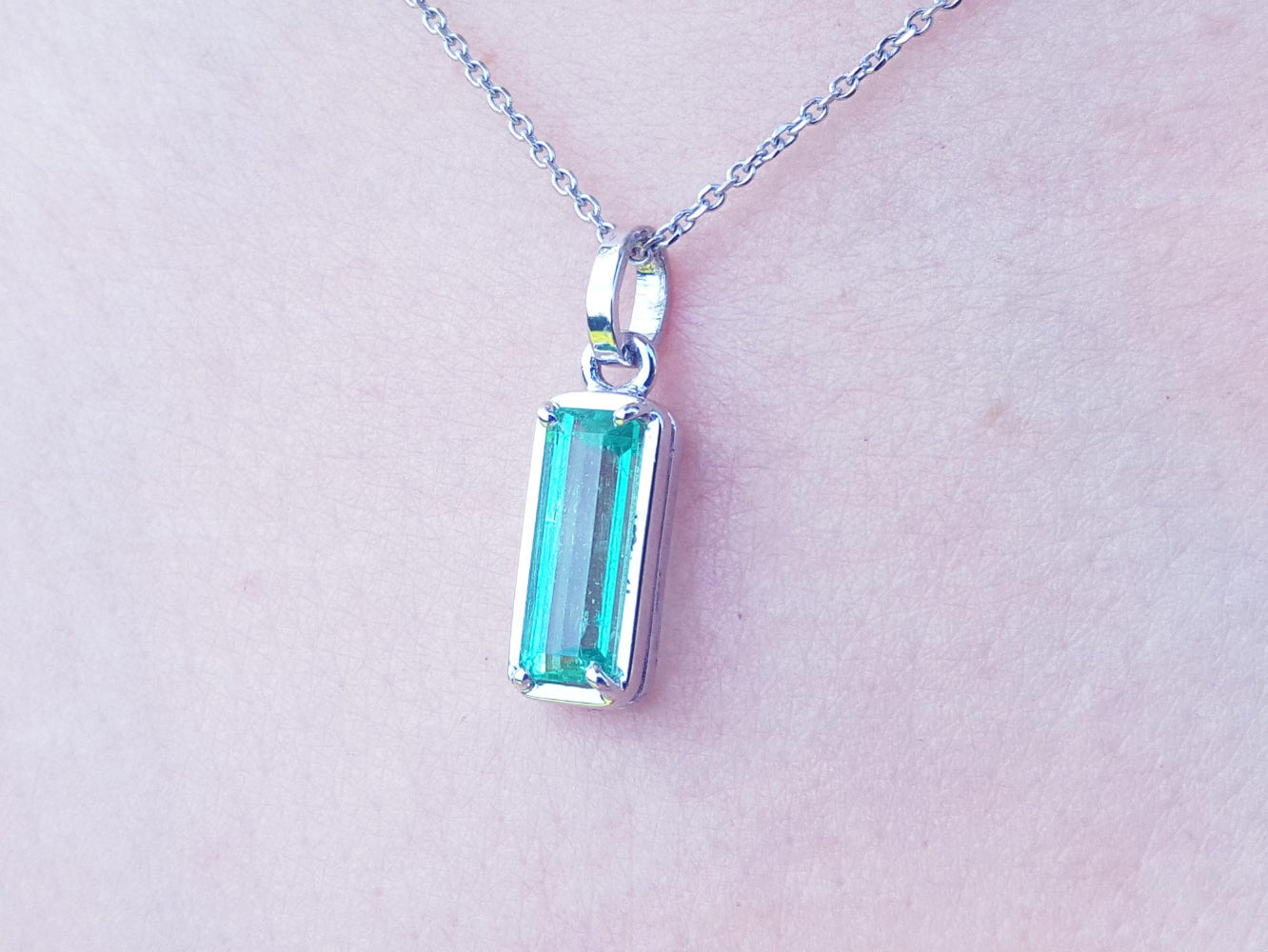 A white gold emerald pendant on a light skin background