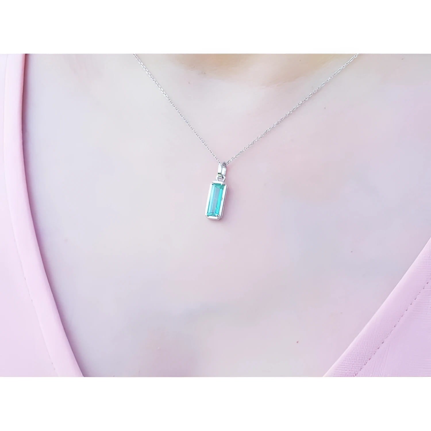Colombian emerald solitaire pendant in 14K white gold, worn on a woman's neck.