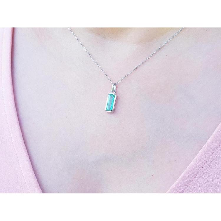 Colombian emerald solitaire pendant in 14K white gold, worn on a woman's neck.