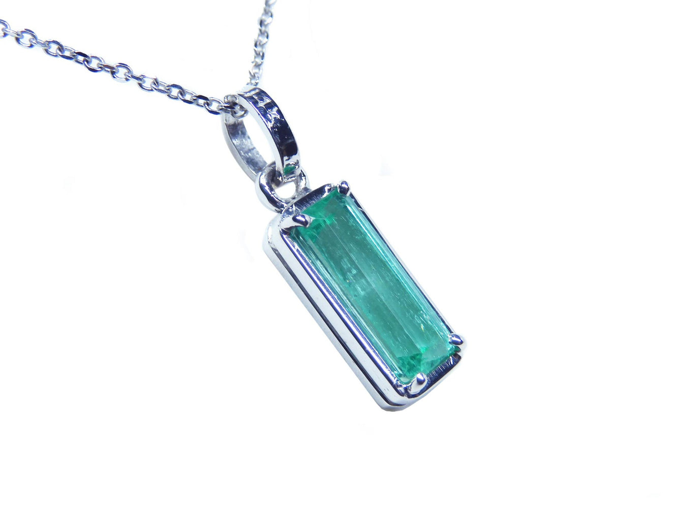 A natural colombian emerald pendant on a white gold chain displaying its topside and gallery profile.