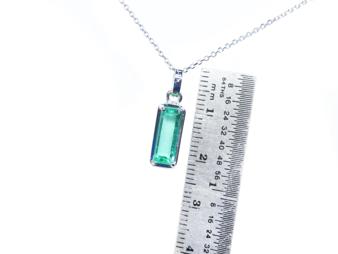 Necklace with a Colombian emerald pendant next to a ruler for scale on a white background