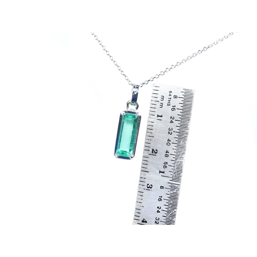 Rectangular emerald cut Colombian emerald solitaire pendant in 14K white gold with ruler for scale.