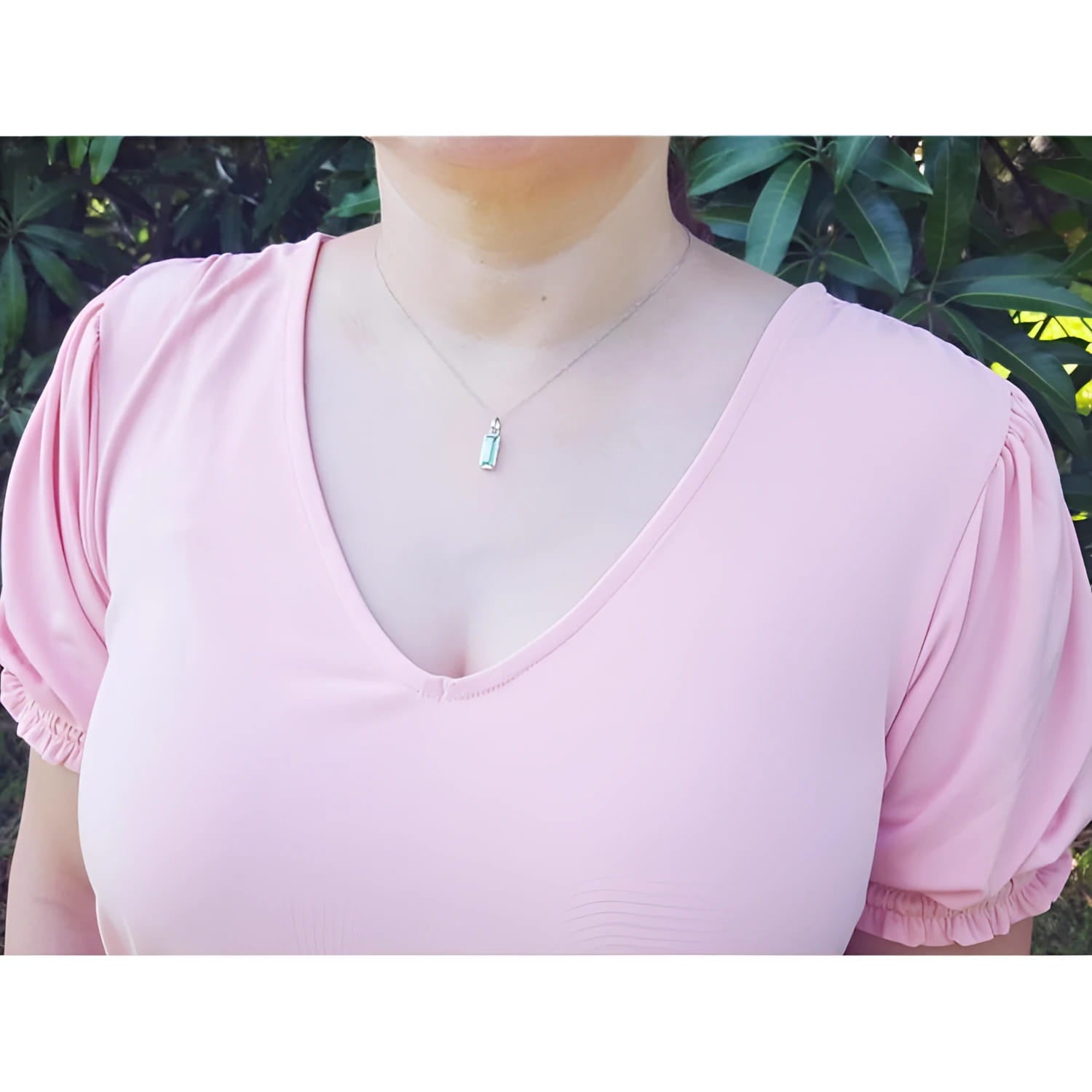 Colombian emerald solitaire pendant in 14K white gold, worn on a woman's neck.