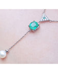 14K white gold necklace with cushion-cut emerald, diamond triangle cluster, and dangling freshwater pearl.