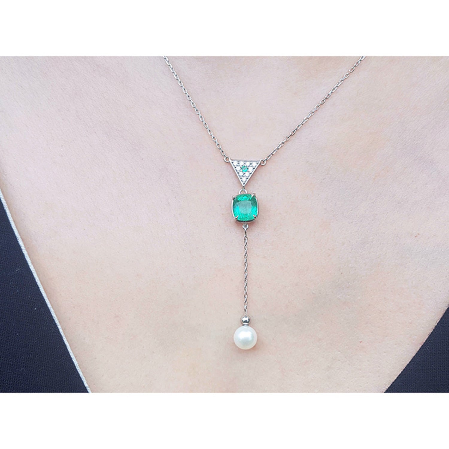 14K white gold necklace with triangle diamond cluster, cushion-cut emerald, and dangling white pearl.