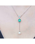 14K white gold necklace with triangle diamond cluster, cushion-cut emerald, and dangling white pearl.