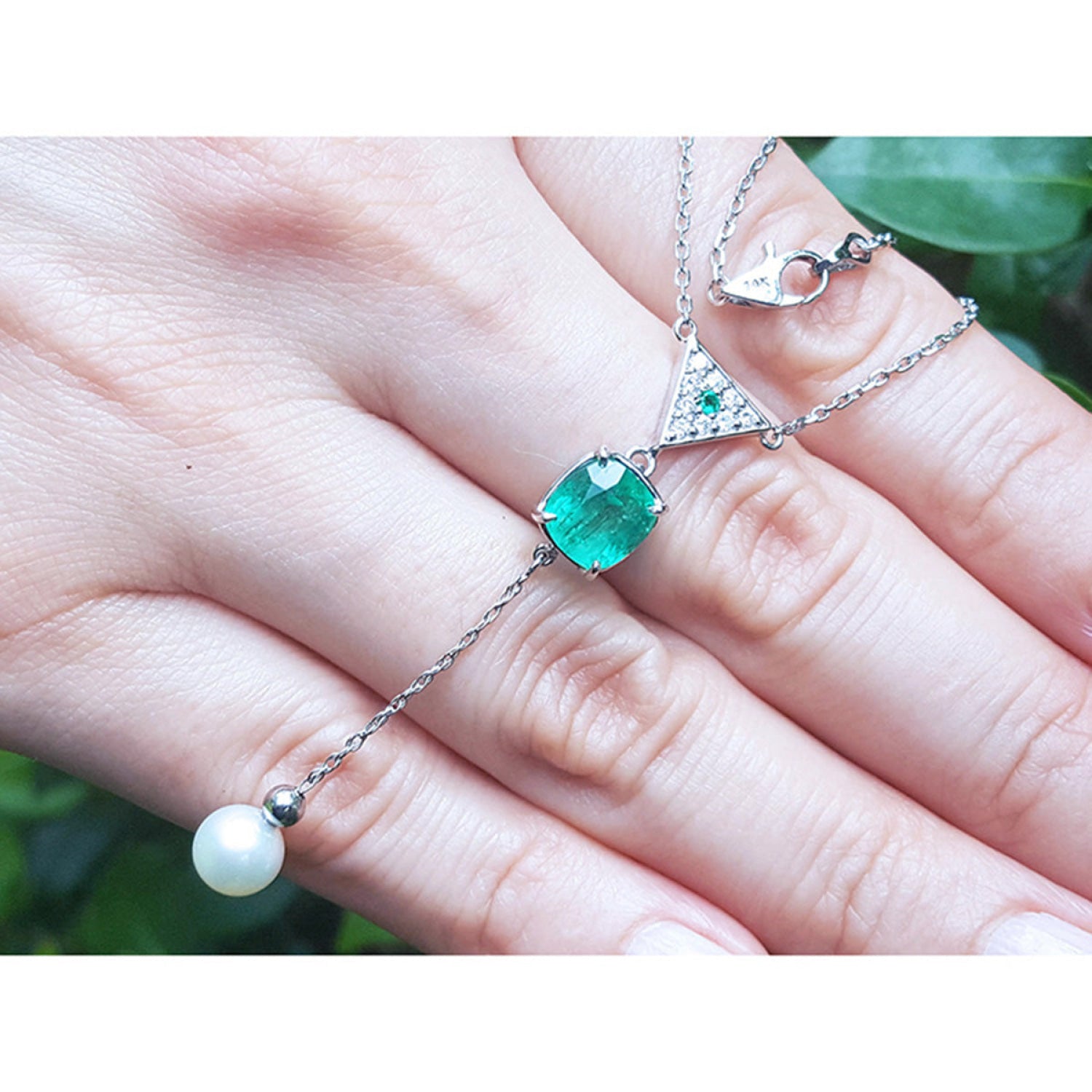 14K white gold necklace with a cushion-cut emerald, diamond triangle cluster, and dangling white pearl.