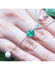 14K white gold necklace with a cushion-cut emerald, diamond triangle cluster, and dangling white pearl.