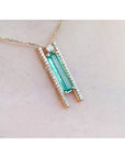 Emerald baguette cut necklace with natural diamonds, 14K yellow gold, and sliding tube bail chain., shown worn on a person's neck against a pale skin background.