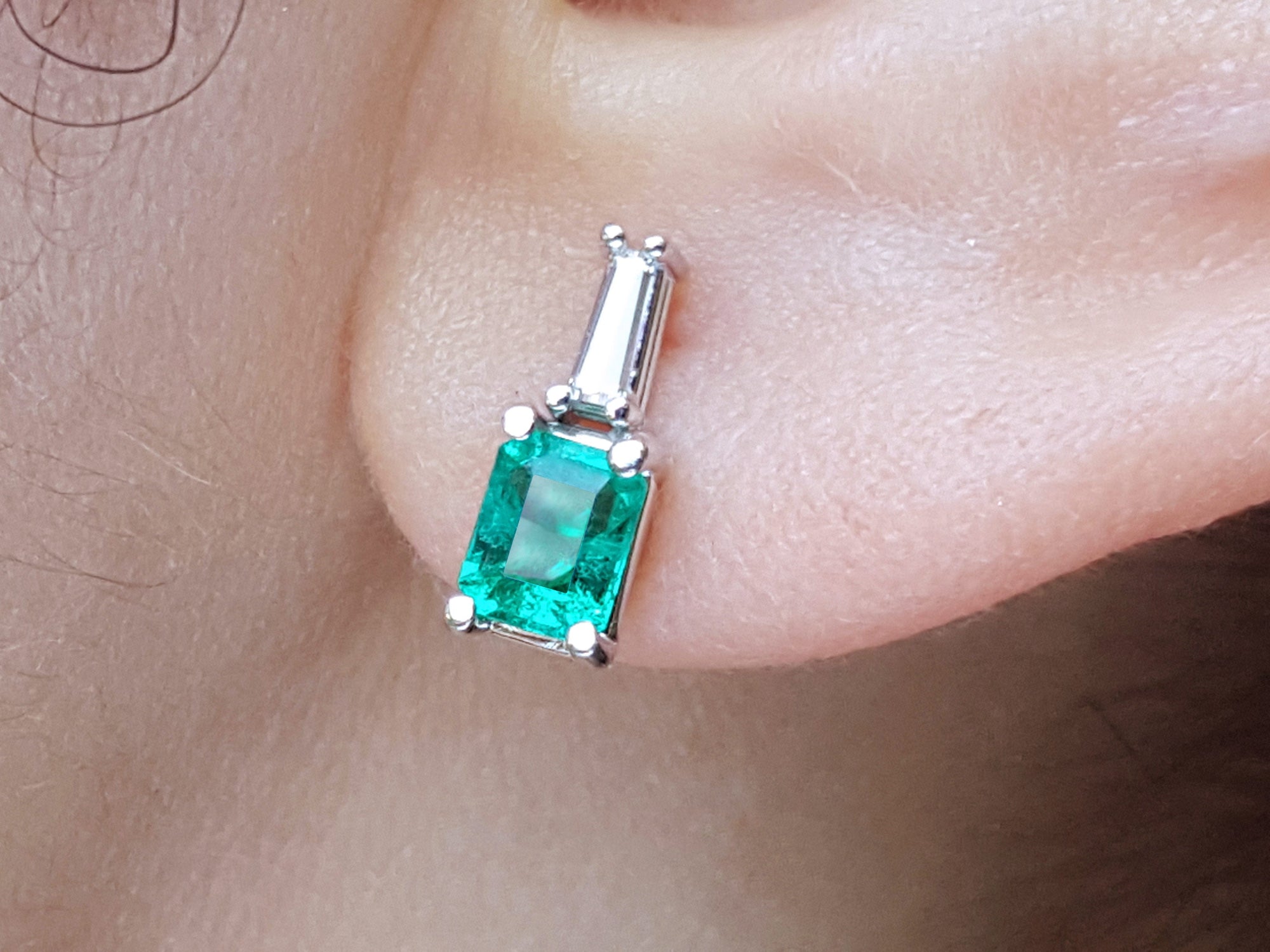close-up of a Colombian emerald and baguette diamond stud earring on an earlobe.
