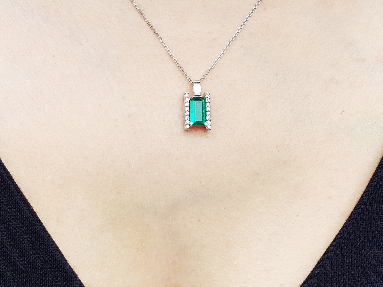 Emerald gemstone pendant on a white gold chain against a beige skin background.