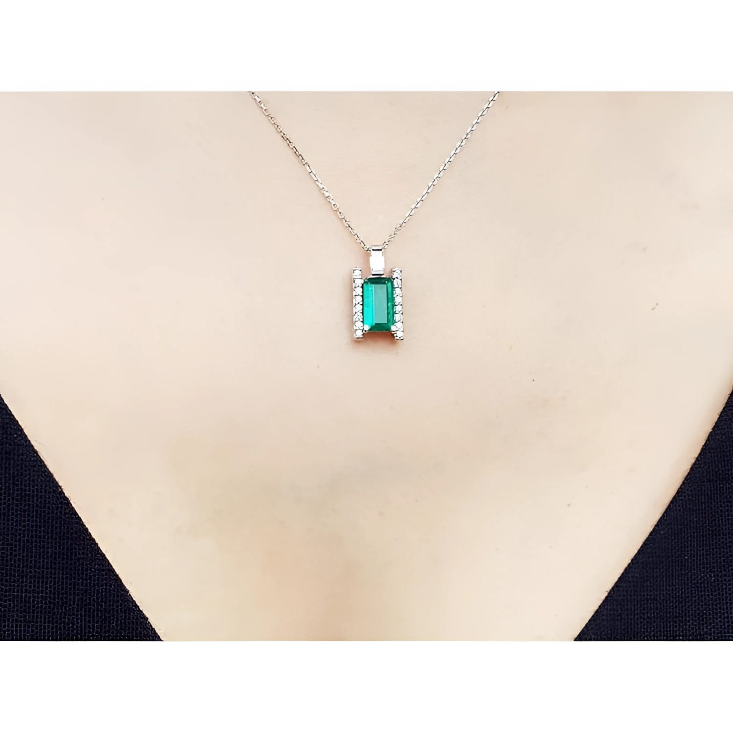 14K white gold baguette cut emerald and diamond pendant necklace on a woman's chest.
