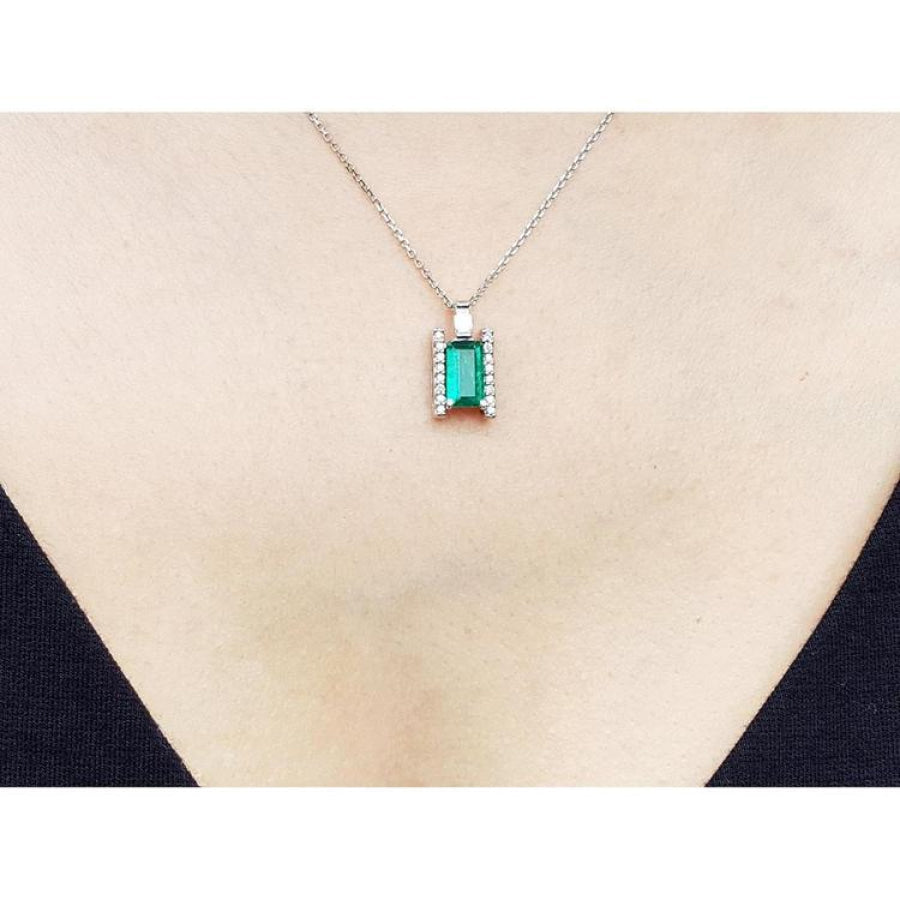 14K white gold baguette cut emerald and diamond pendant necklace on a woman's chest.