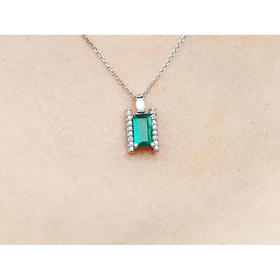 Emerald gemstone pendant on a white gold chain against a beige skin background.