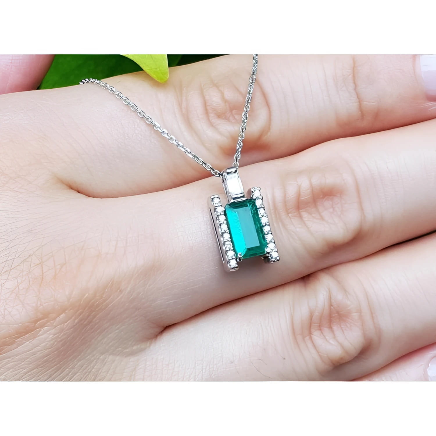 14K white gold emerald and diamond baguette cut pendant necklace on a hand.