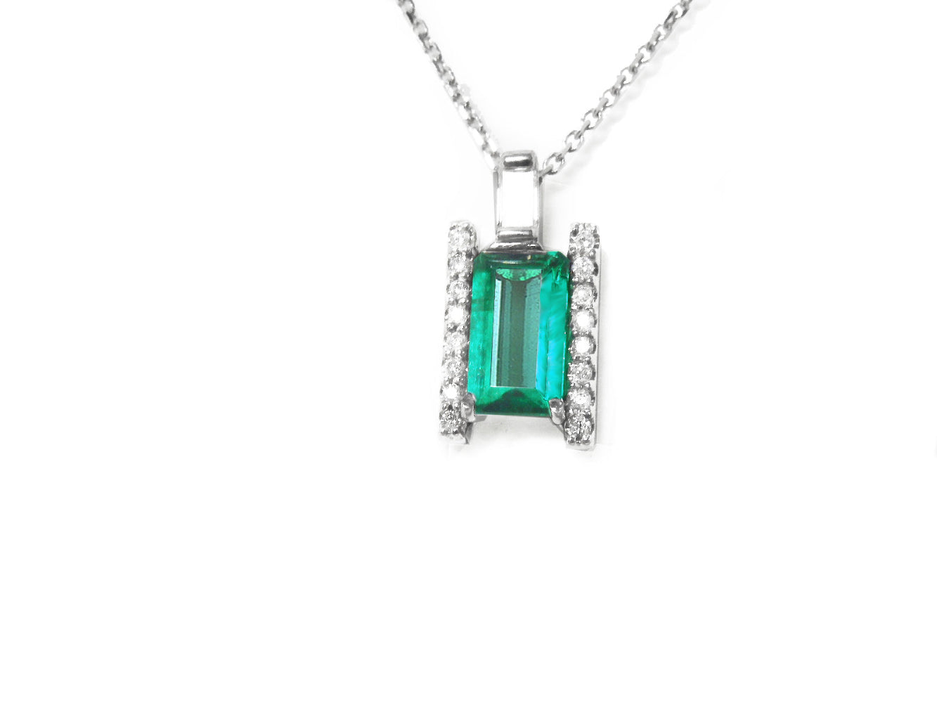 A natural emerald gemstone pendant with diamond accents on a topside view position.