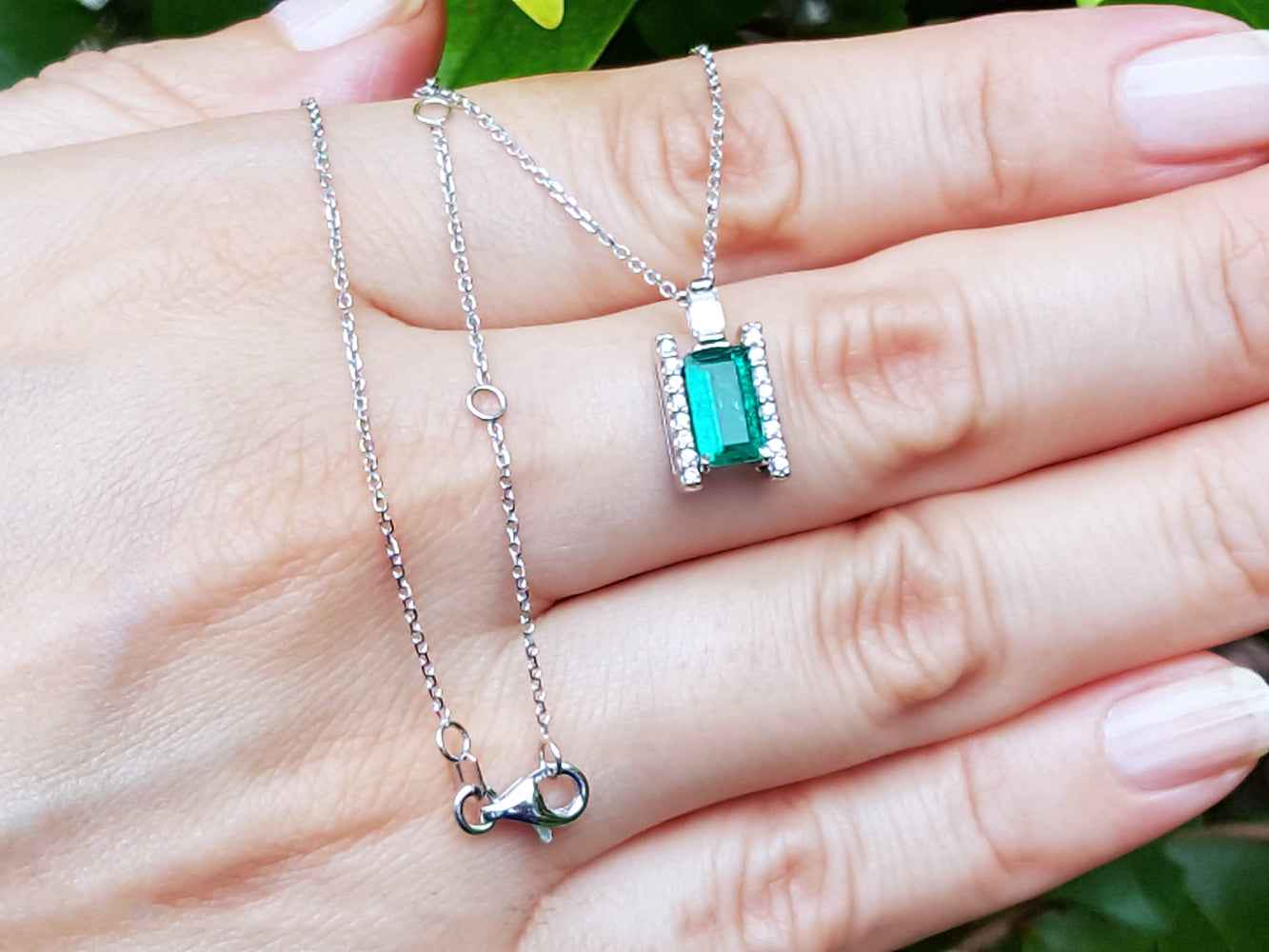 White gold necklace with a natural emerald gemstone pendant on a hand against a natural background.