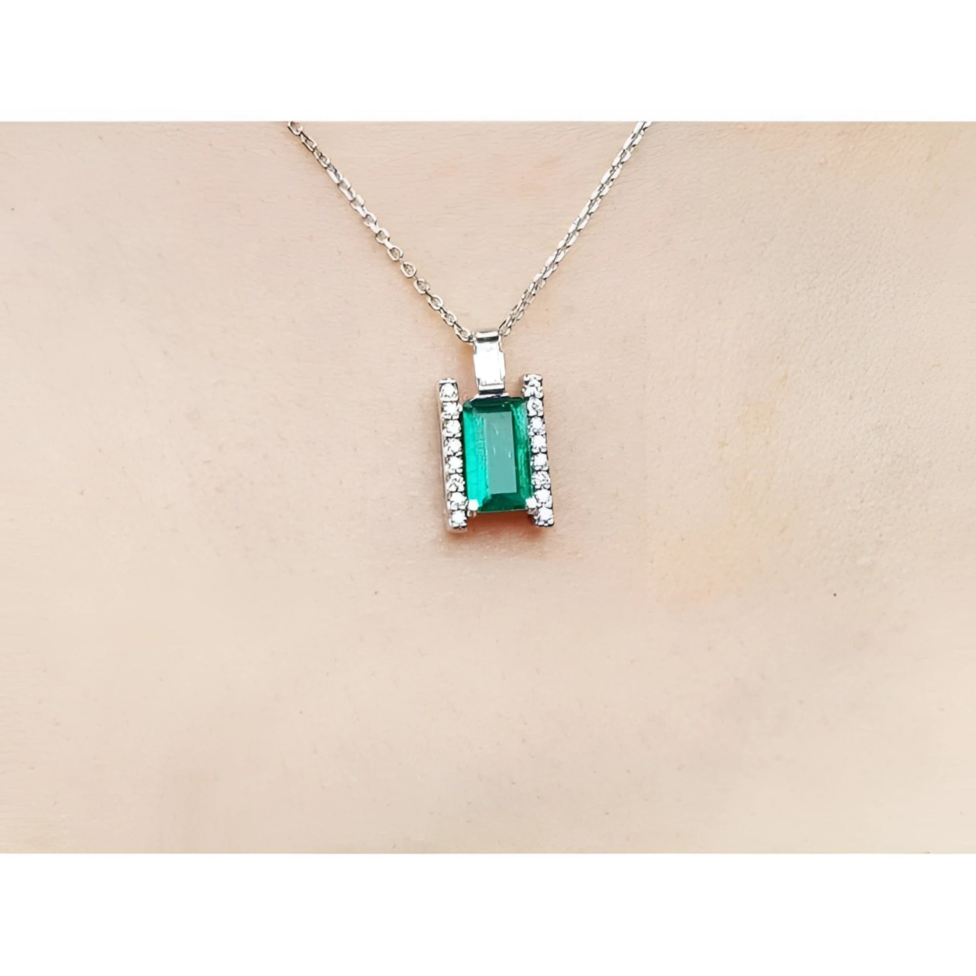Emerald gemstone pendant on a white gold chain against a beige skin background.