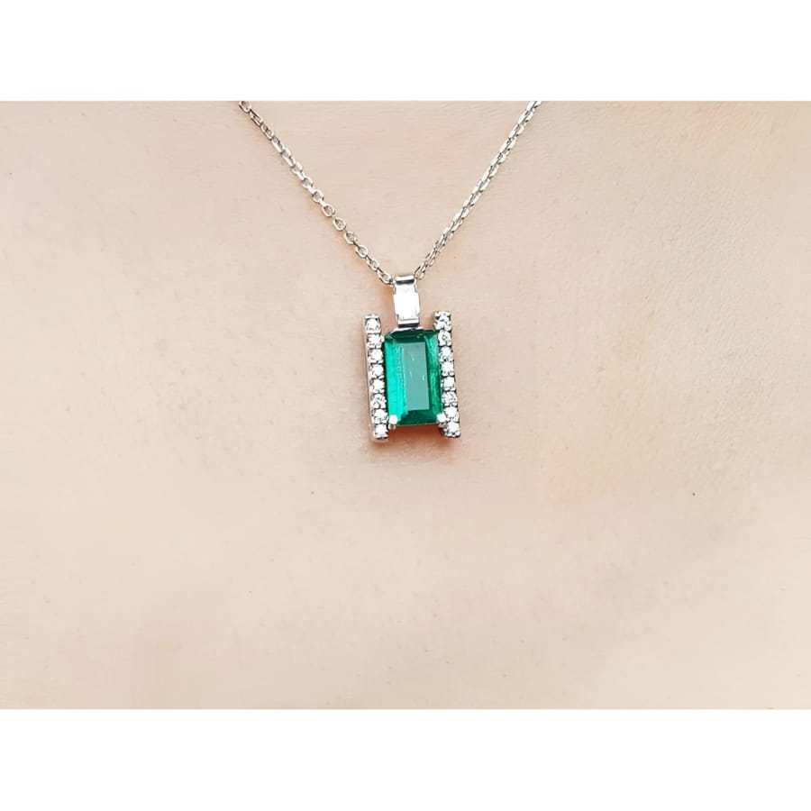 Emerald gemstone pendant on a white gold chain against a beige skin background.