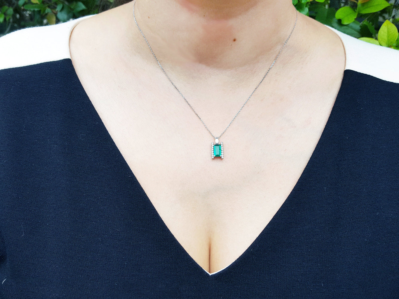A woman wearing a necklace with a natural baguette cut emerald on a plain natural background.