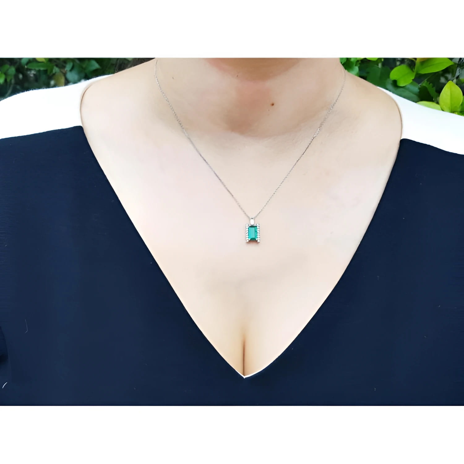 Baguette cut emerald and diamond pendant necklace in 14K white gold, worn on a woman's chest.