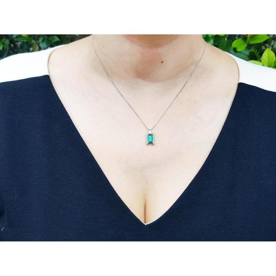 Baguette cut emerald and diamond pendant necklace in 14K white gold, worn on a woman's chest.