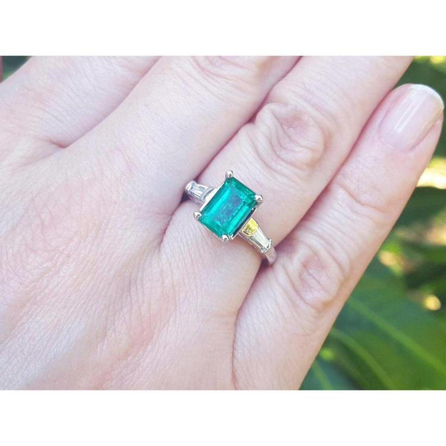 18K gold ring with a 2.21 ct deep bluish-green emerald and tapered baguette diamonds on a hand.