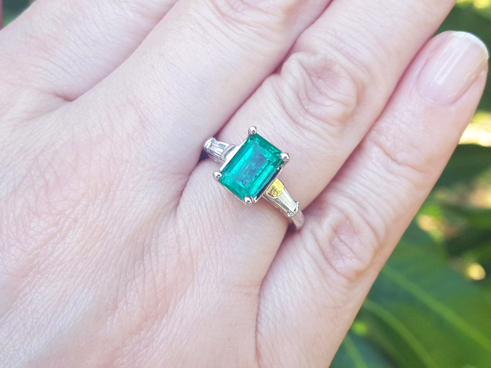 Emerald ring on a hand with a blurred green background.