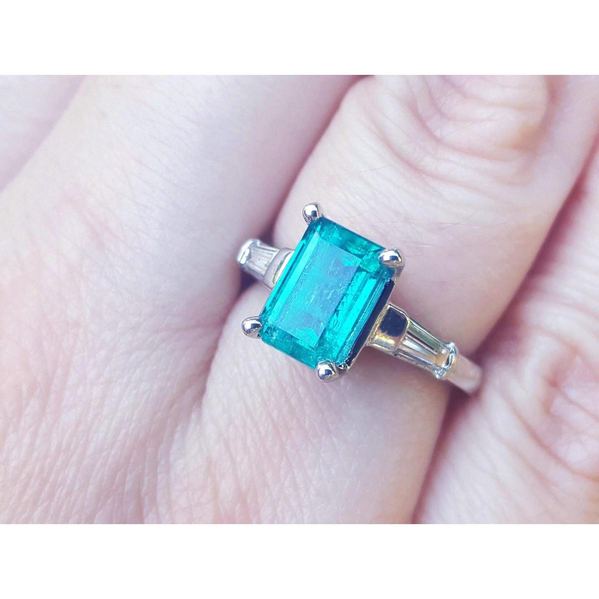 A three stone emerald and baguette side diamond ring in white gold on a finger.