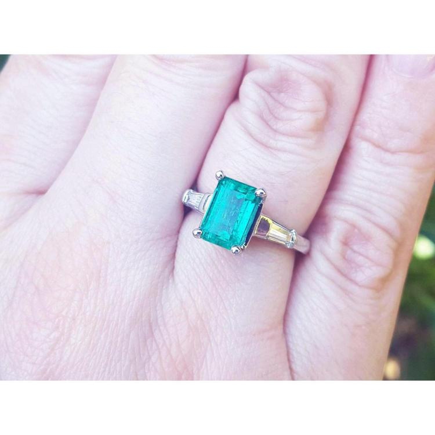 18K gold ring with a deep bluish-green emerald and tapered baguette side diamonds on a hand.