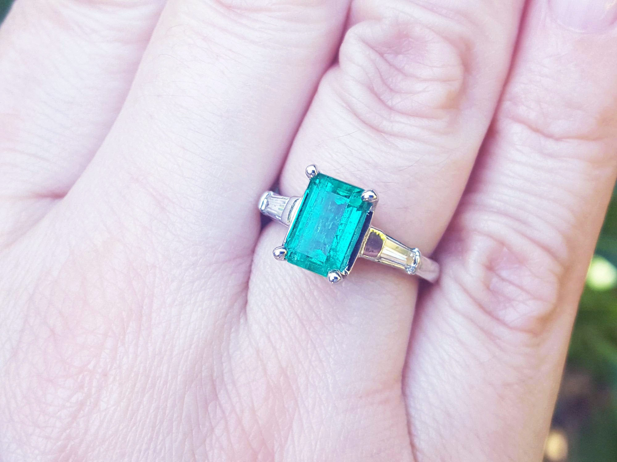 Ring with a natural emerald and baguette diamond for women on a finger.