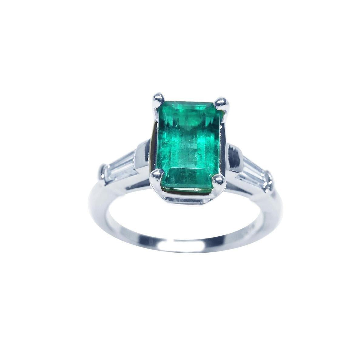 A 18k white gold three stone emerald and baguette side diamond ring on a top view and side profile position.