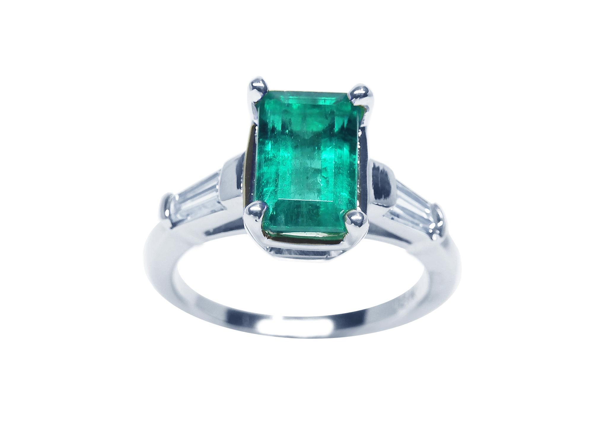 A 18k white gold three stone emerald and baguette side diamond ring on a top view and side profile position.