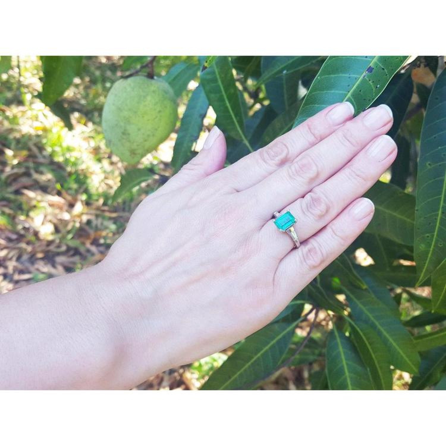 18K gold ring with a 2.21 ct deep bluish-green emerald and baguette side diamonds on a hand.