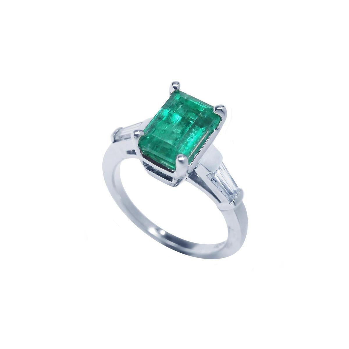 This 18k white gold emerald ring with side baguette diamonds is on a tilted position displaying a top view and side profile.
