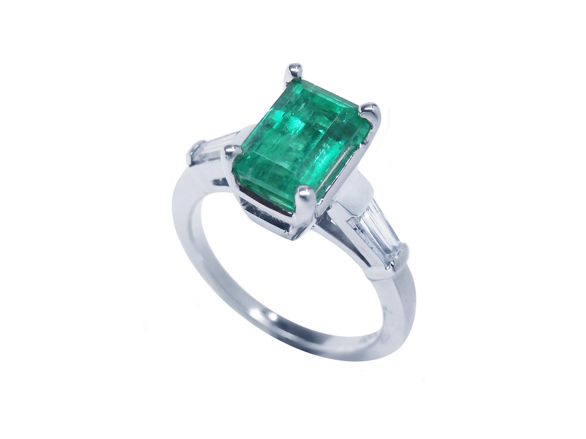 This 18k white gold emerald ring with side baguette diamonds is on a tilted position displaying a top view and side profile.