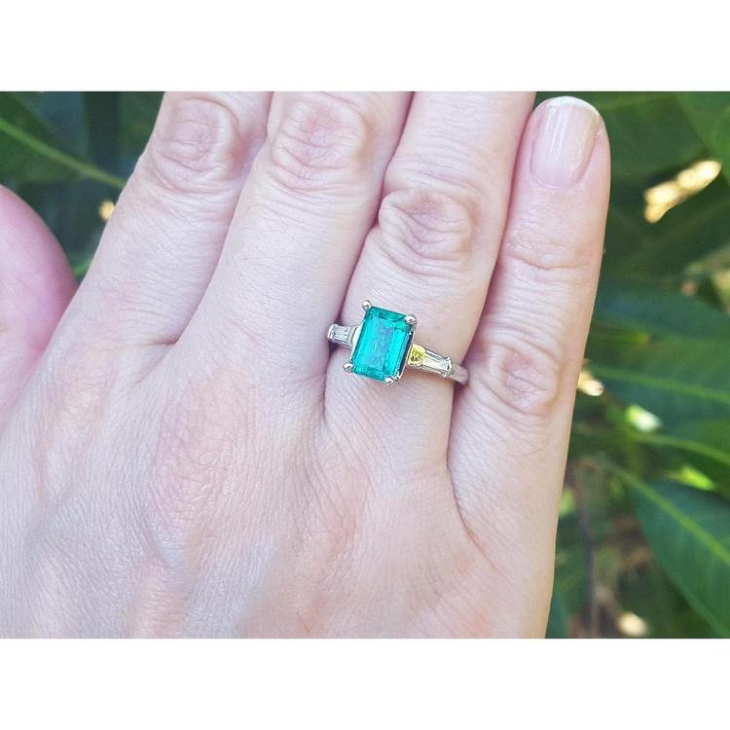 18K gold ring with a deep bluish-green emerald and tapered baguette diamonds on a hand.