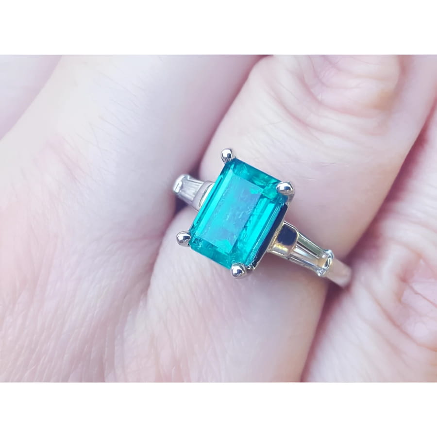 A three stone genuine emerald and baguette side diamond ring in white gold on a finger.