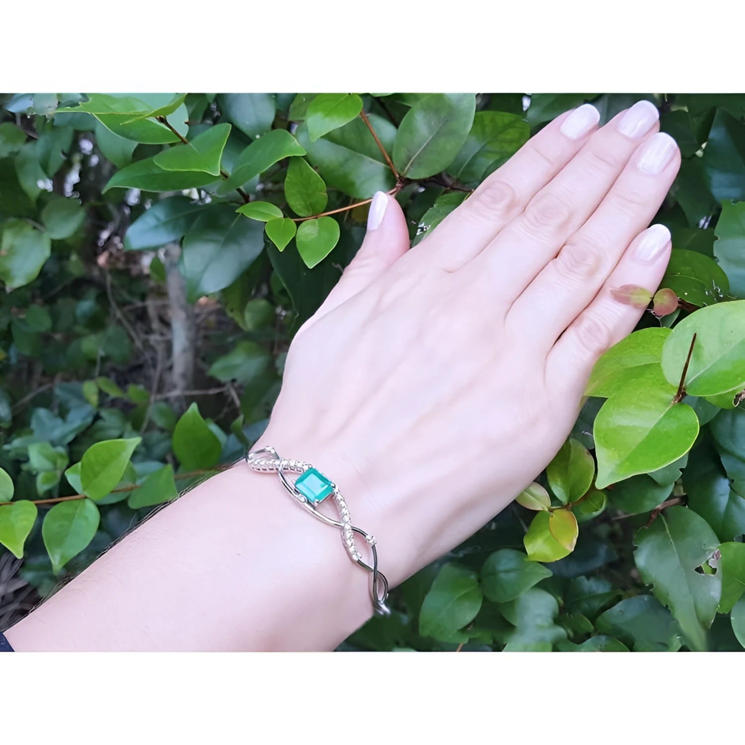 Emerald-cut emerald and natural diamond bangle bracelet in 14K white gold on a woman's wrist.