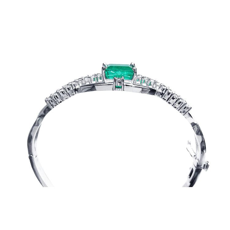 14K white gold bangle bracelet with a central emerald-cut green emerald and diamond accents.